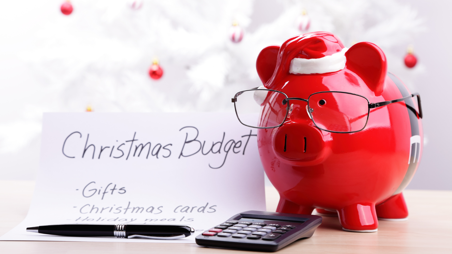 Red piggy bank wearing glasses next to a Christmas budget list and a calculator.