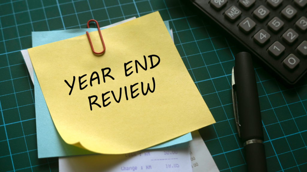 Yellow sticky note with the text 'YEAR END REVIEW' clipped to a blue paper on a green grid background.